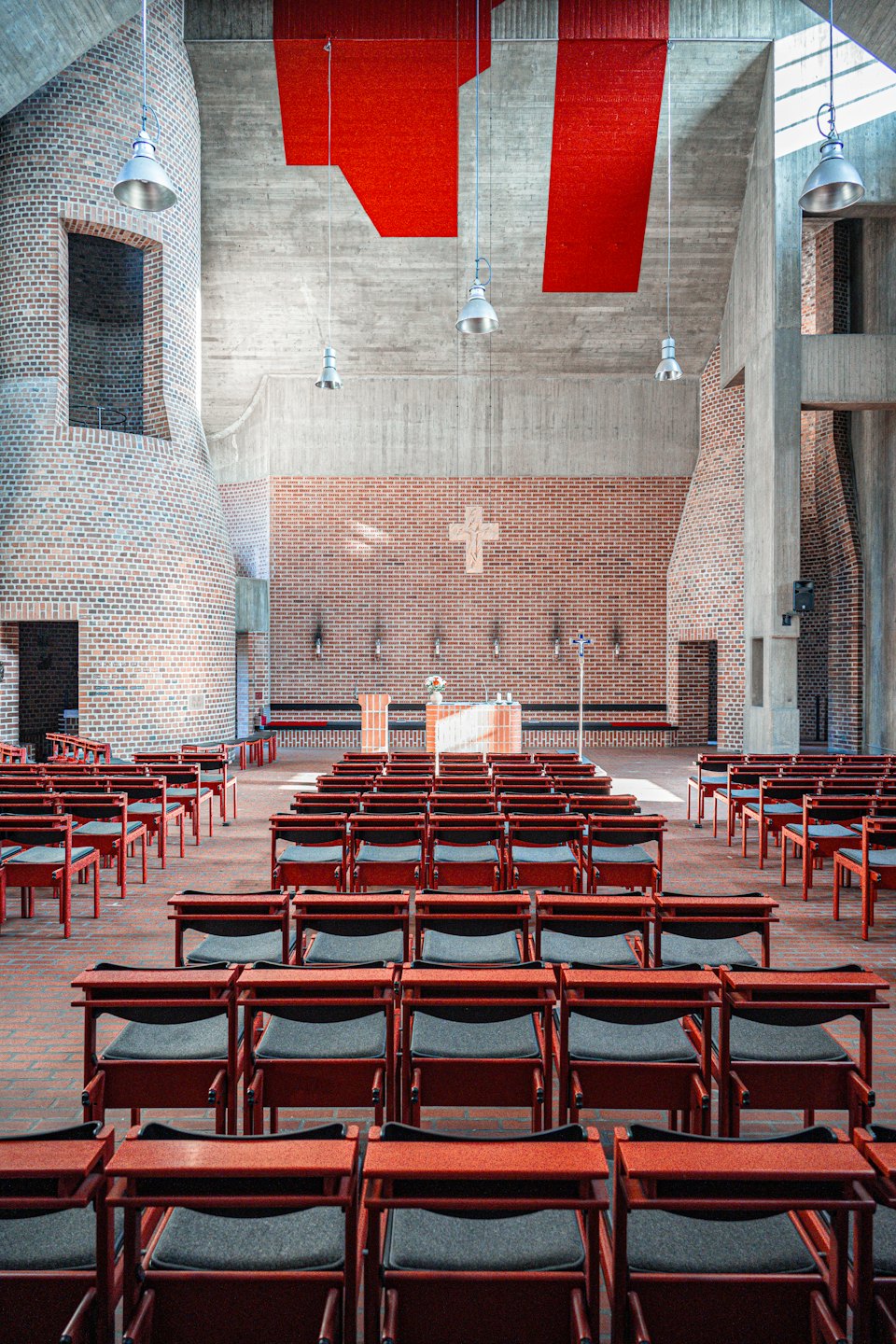 Rader av röda stolar vända mot ett tegelaltare i en kyrka.