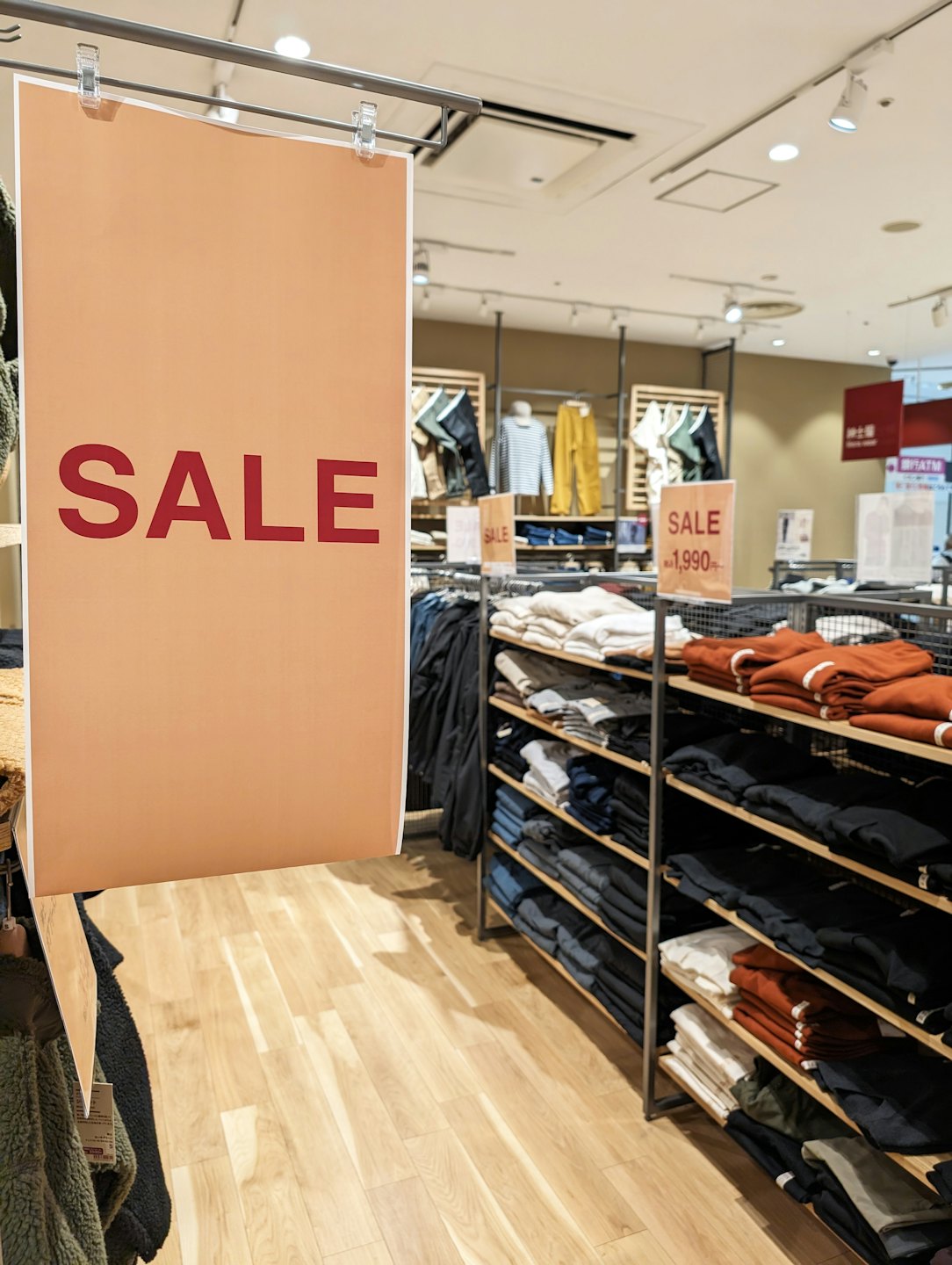 Persikofärgad "REA"-skylt i en klädbutik med vikta kläder.