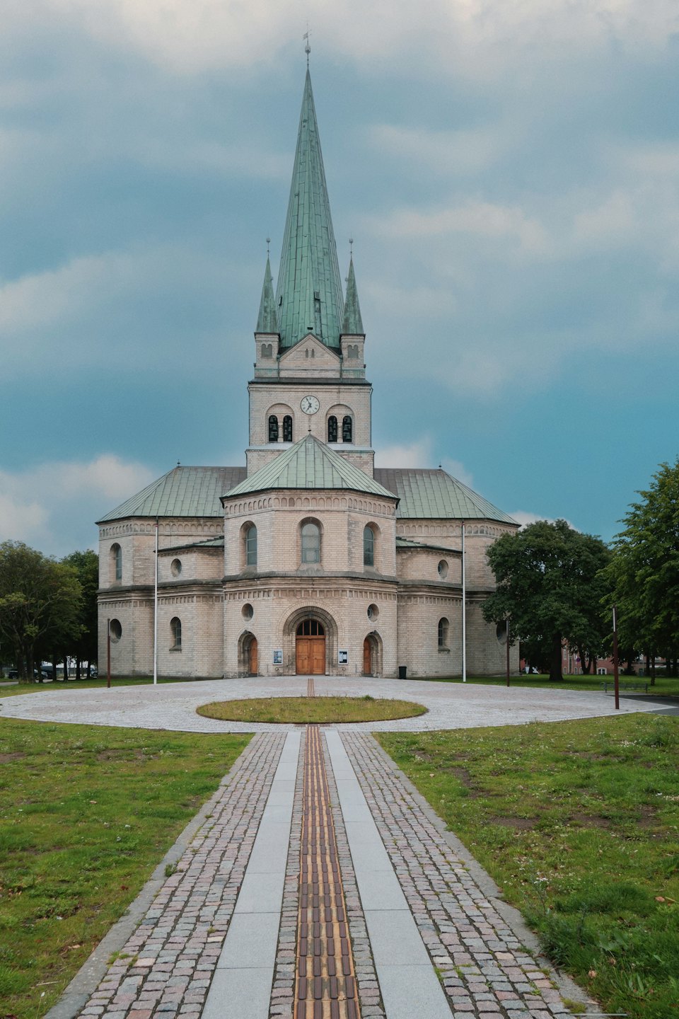 En stenkyrka med gröna spiror och en asfalterad gångväg.