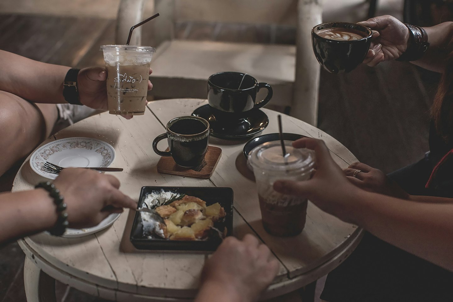 Vänner delar kaffe och dessert runt ett träbord på ett café.